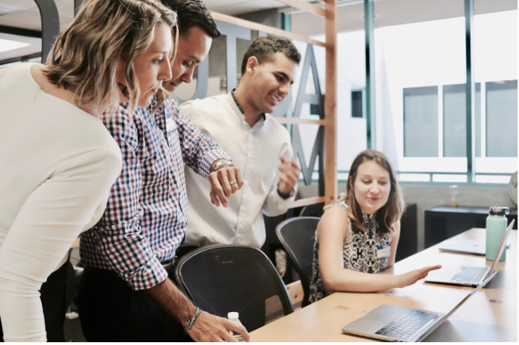 four people looking at a laptop on table